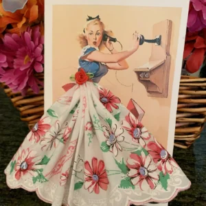 Vintage paper doll in a floral dress with a bow in her hair.