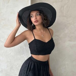 Young woman in a black crop top and skirt posing against a plain wall.