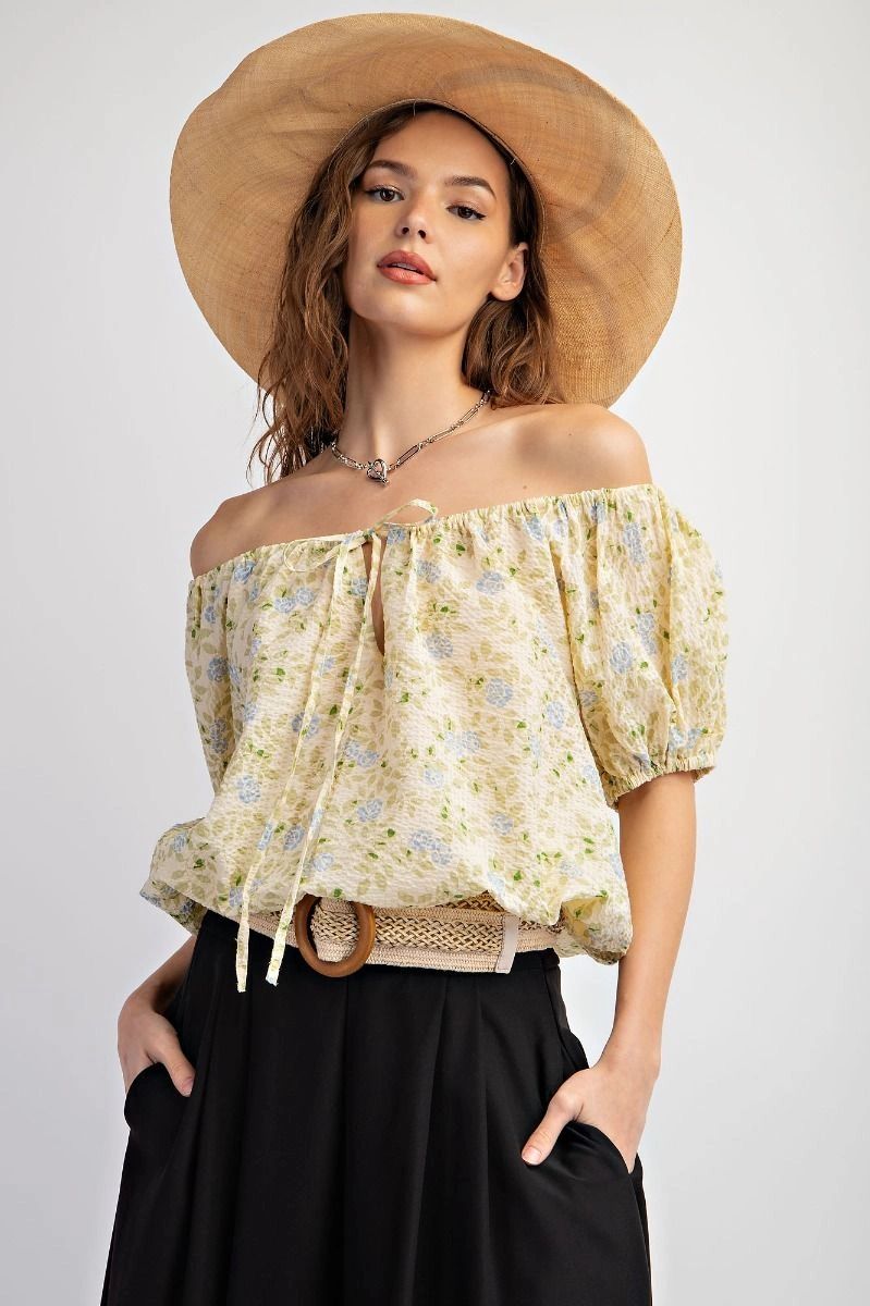 Woman wearing a floral off-shoulder blouse and straw hat.