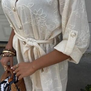 Close-up of a person wearing an elegant, embroidered cream-colored dress with a tied belt.