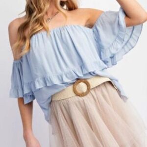 Woman wearing a light blue off-shoulder ruffled top and beige skirt with a belt.