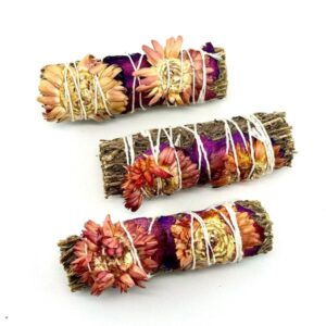 Three decorative smudge sticks wrapped with dried flowers and herbs.