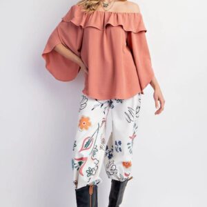 Woman wearing a ruffled off-shoulder top and floral pants with black boots.