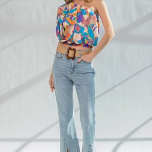 Woman in colorful top and light blue jeans posing indoors.