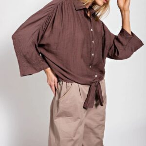 Woman wearing a loose brown button-up blouse with beige pants.