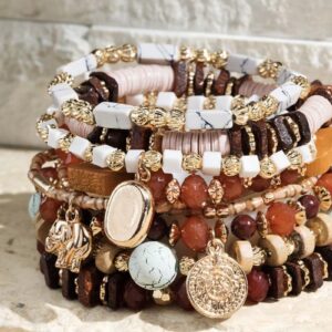 Stack of various beaded and shell bracelets on a textured surface.