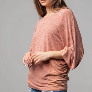 Woman wearing a loose pink long-sleeve top with ruched sleeves.