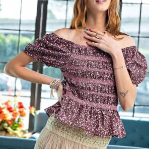 Woman wearing a stylish off-shoulder floral top and a beige skirt indoors.