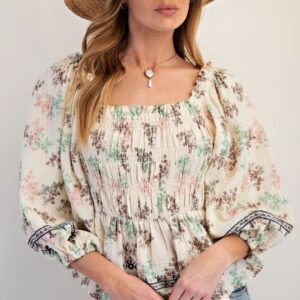 Woman wearing a floral, smocked blouse with puffed sleeves.