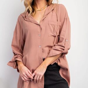Woman wearing a loose pink button-up shirt with rolled sleeves.