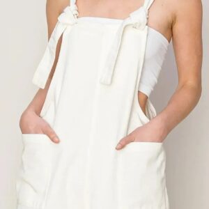 Woman wearing a white sleeveless dress with pockets and shoulder ties.