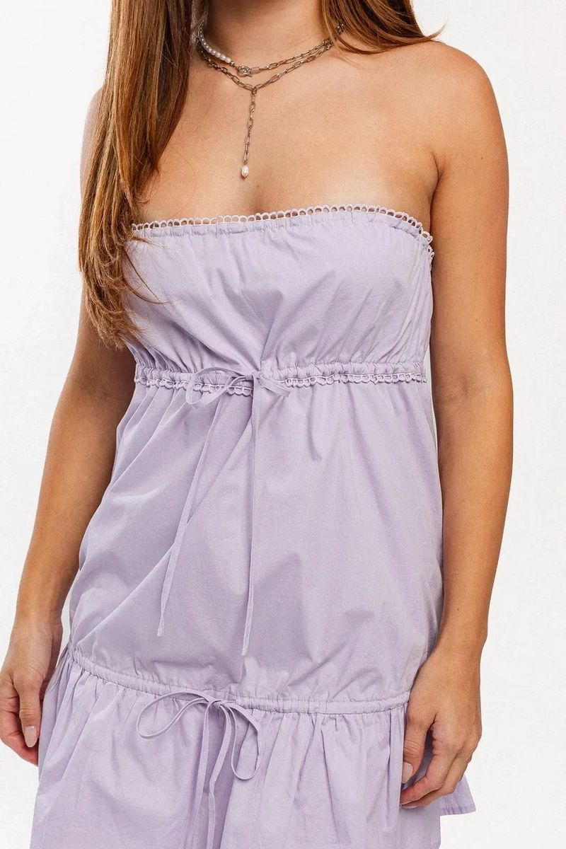 Woman wearing a strapless light purple dress with a cinched waist.