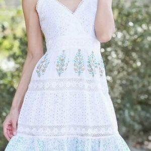 Woman wearing a white summer dress with blue floral embroidery.