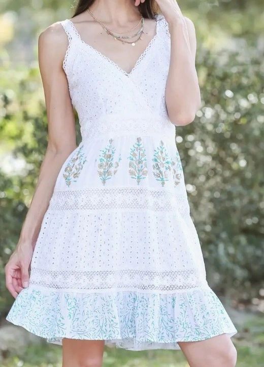 Woman wearing a white summer dress with blue floral embroidery.