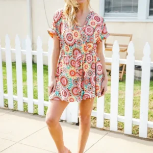Woman in a colorful floral dress standing by a white picket fence.