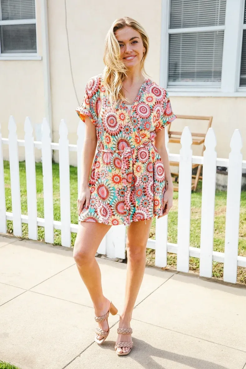Woman in a colorful floral dress standing by a white picket fence.