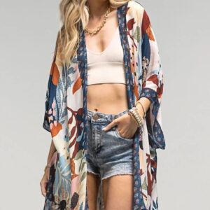 Woman wearing a colorful kimono over a crop top and denim shorts.