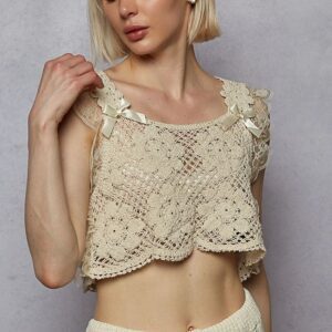 Woman wearing a beige crocheted crop top and light pants.