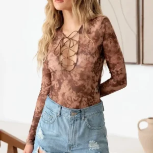 Woman wearing a brown floral lace-up bodysuit with long sleeves and denim shorts.