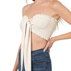 Woman wearing a white strapless crop top with a bow detail and blue jeans.